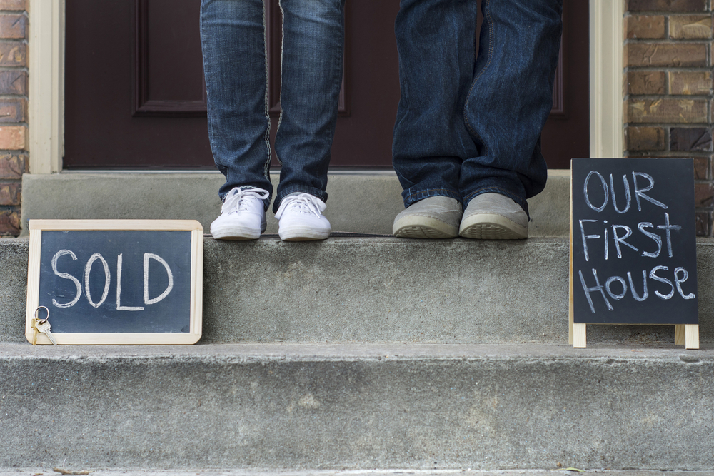 Two people standing on a porch with chalk signs that read "sold" and "our new home"
