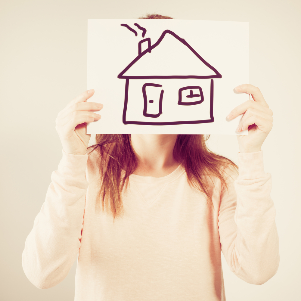 a woman holds up a piece of paper in front of her head with a house drawn on it