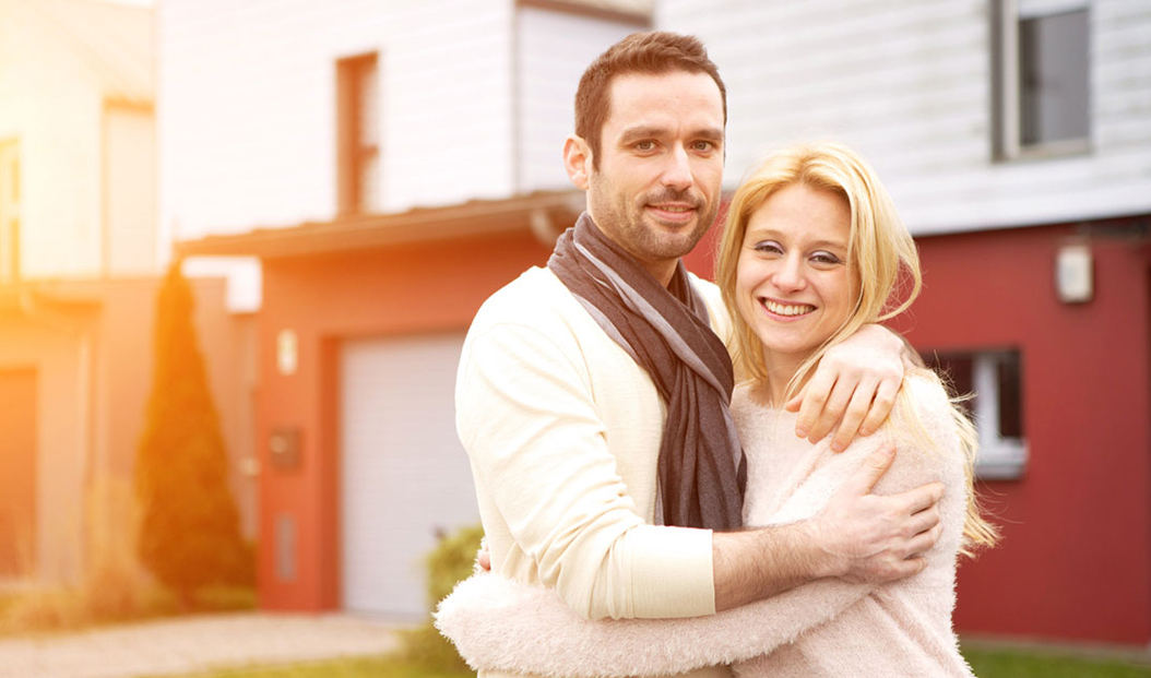 a couple embraces in front of their home