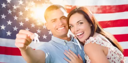 a couple holding keys to new house in front of an American flag