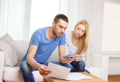 a young couple sits on a couch looking at documents and holding a calculator