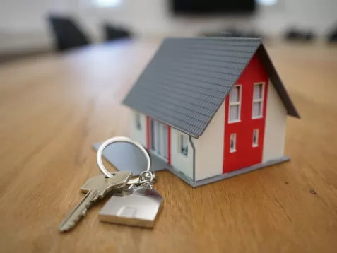 a key lays beside a small toy house on a wooden table. 